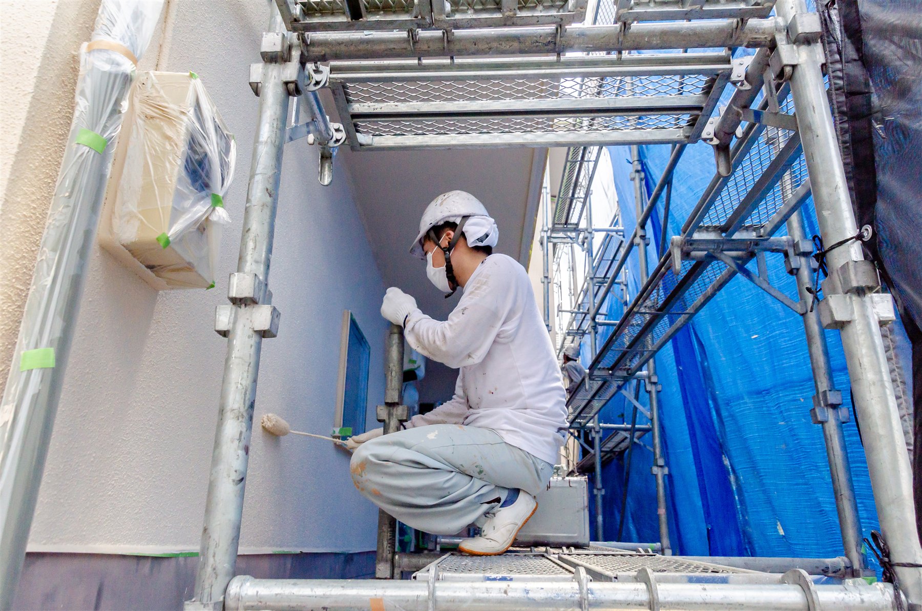 足場の上で住宅外壁を塗装する作業者